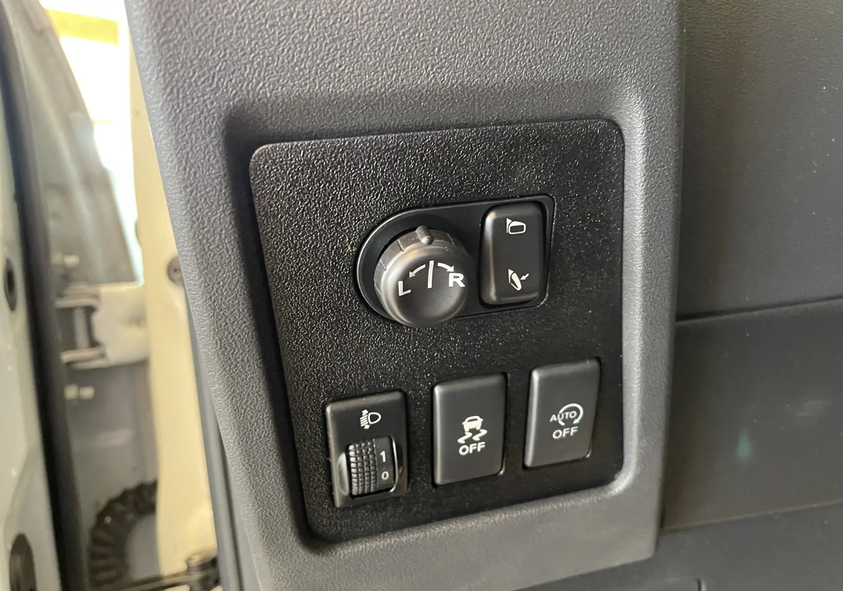 Panneau de commandes noir côté gauche du tableau de bord d'un Nissan Qashqai blanc, avec boutons de réglage des rétroviseurs et aides à la conduite.