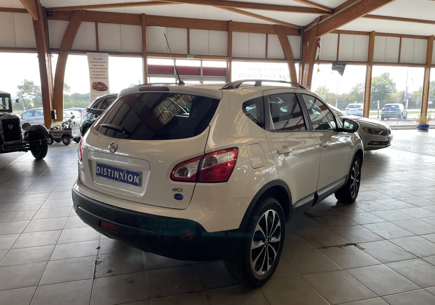 Vue 3/4 arrière droite d'un Nissan Qashqai blanc 2013 en showroom, avec jantes alliage et vitres teintées.