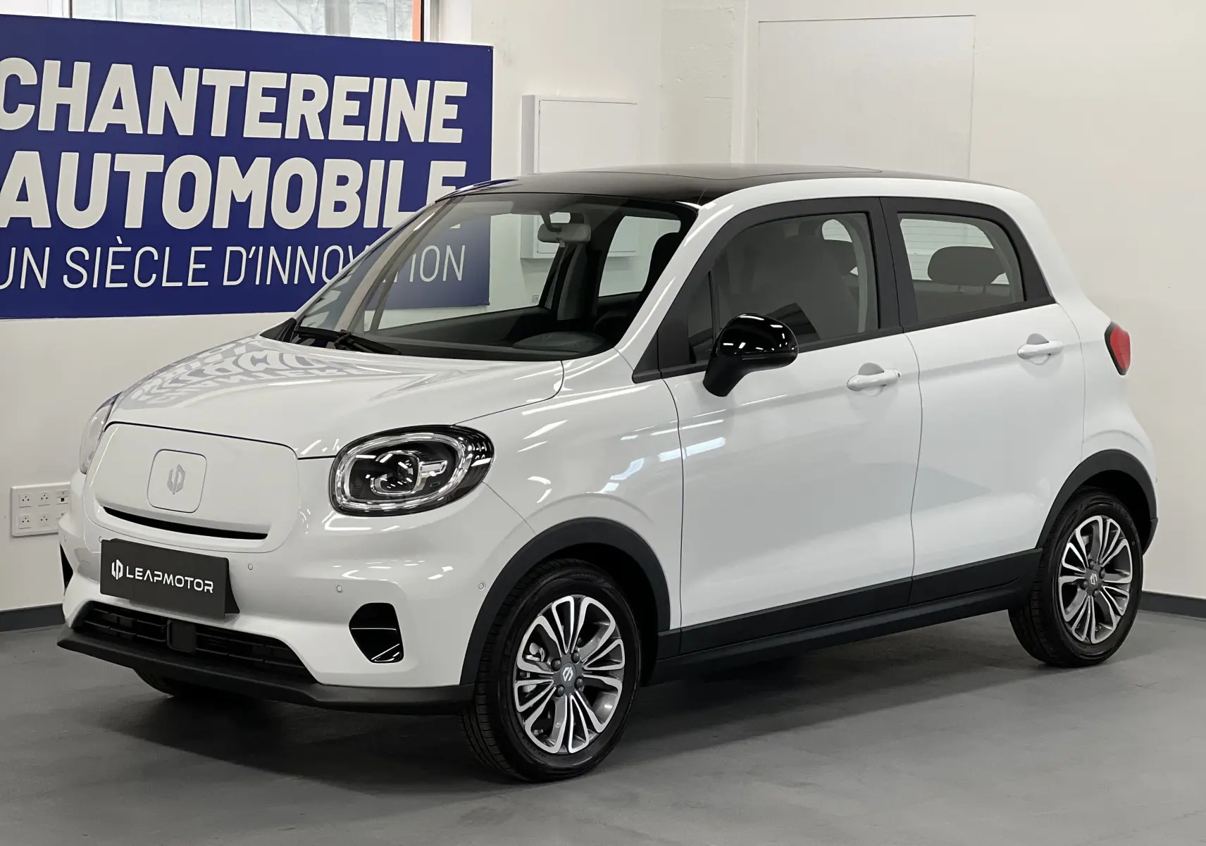 Vue 3/4 avant droite d'une Renault ZOE blanche électrique 2024 avec toit noir et jantes stylisées en intérieur showroom.