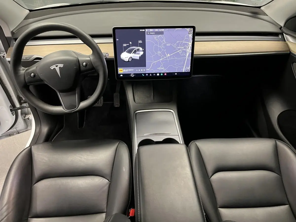 Vue intérieure avant de la Tesla Model Y blanche avec tableau de bord minimaliste et écran tactile central affichant la navigation.