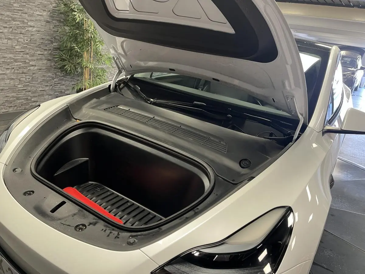 Vue 3/4 avant droit d'une Tesla Model Y blanche avec capot ouvert dévoilant le coffre avant vide.