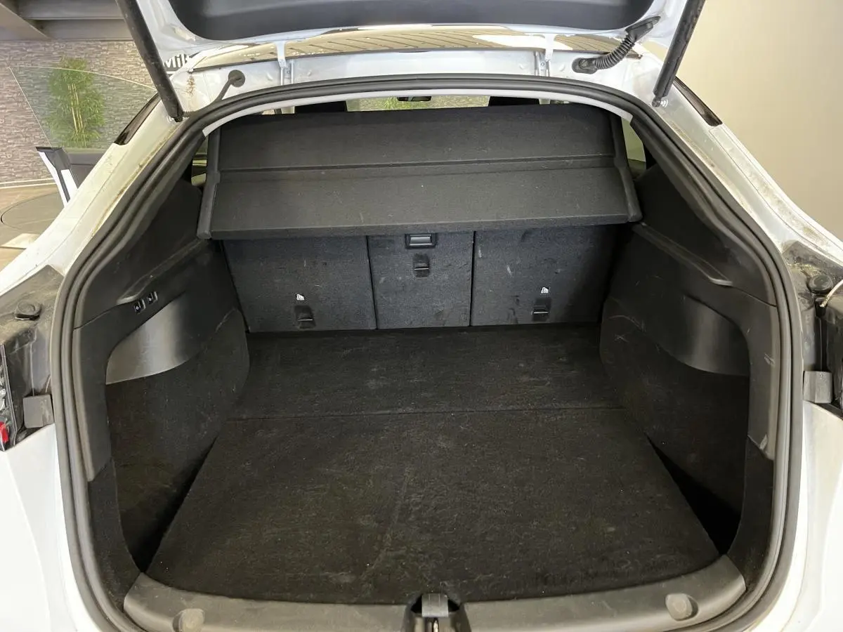 Coffre ouvert d'une Tesla Model Y blanc nacré, montrant l'espace de chargement et la tablette de séparation noire.
