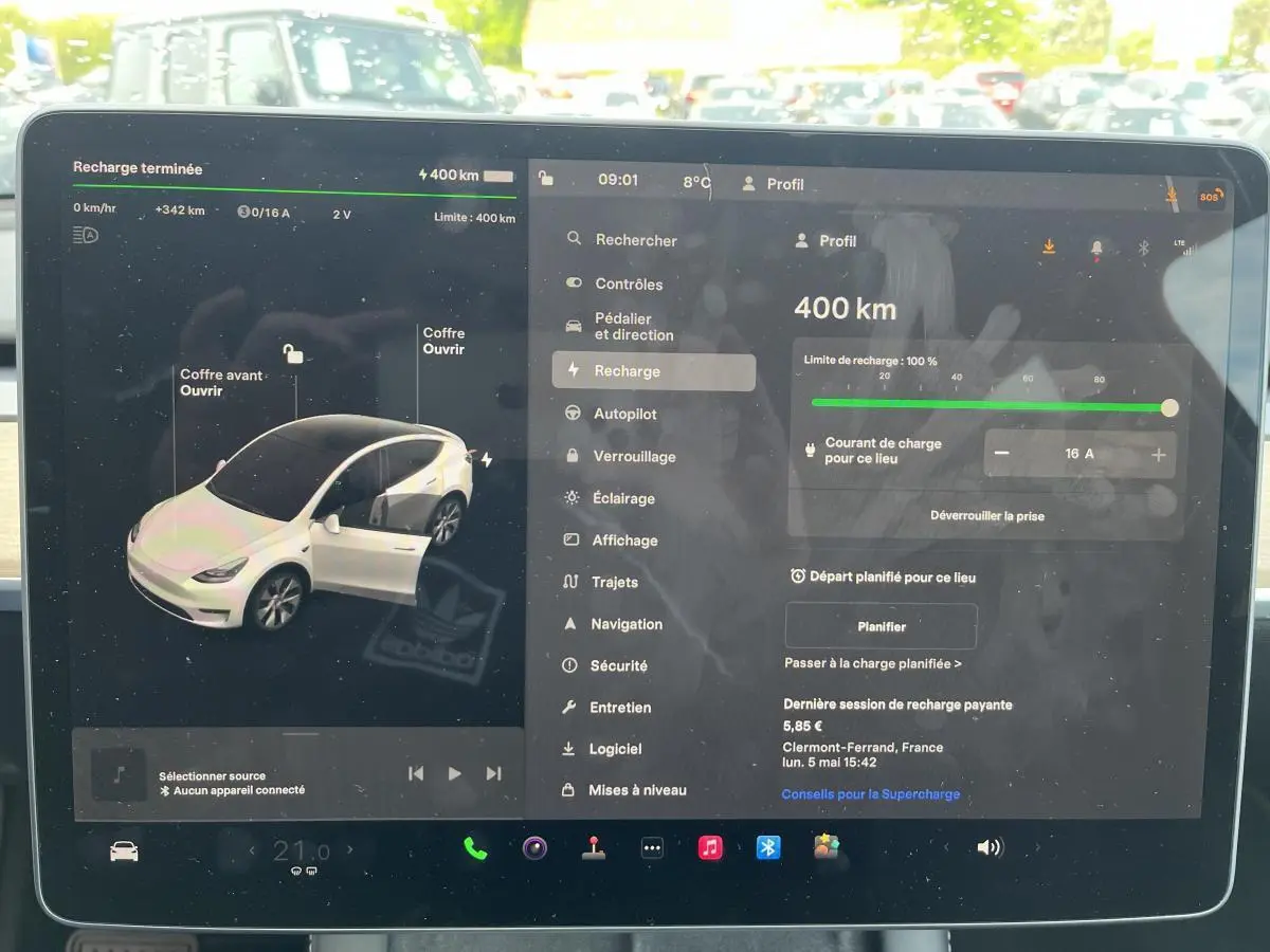 Écran tactile intérieur montrant l'interface de recharge d'une Tesla Model Y blanche en vue de face.