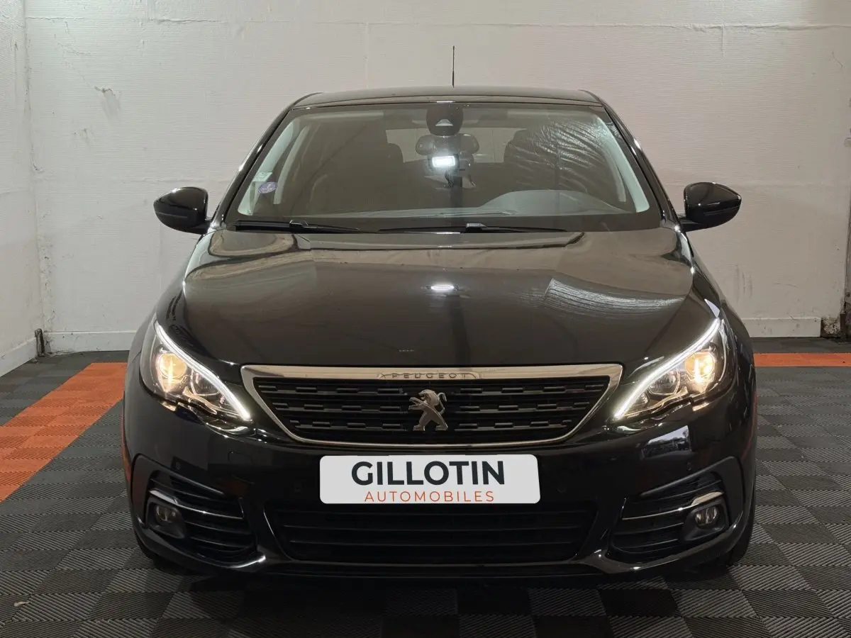 Vue frontale d'une Peugeot 308 noire avec phares allumés et calandre au lion distinctif.