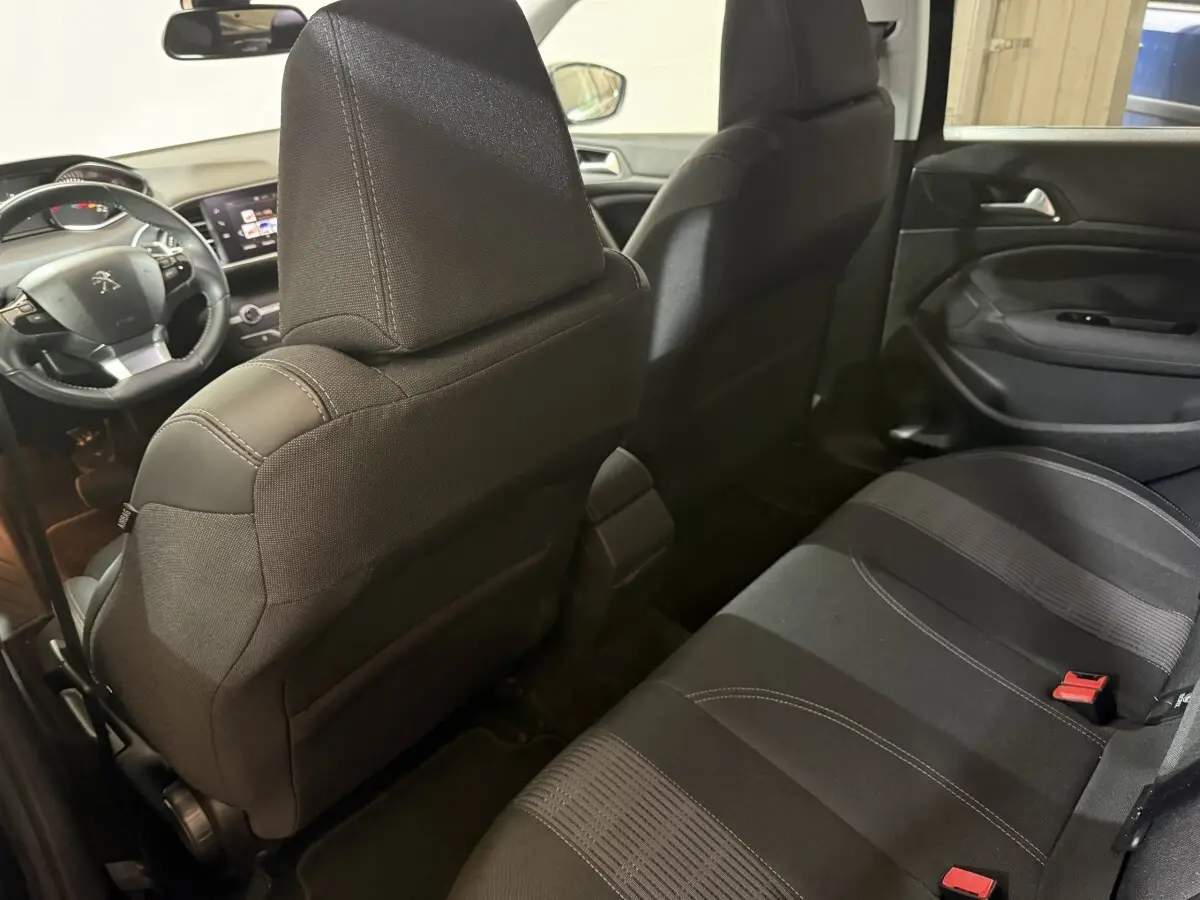 Vue intérieure arrière côté droit de la Peugeot 308 noire, montrant les sièges tissu et le tableau de bord avant.