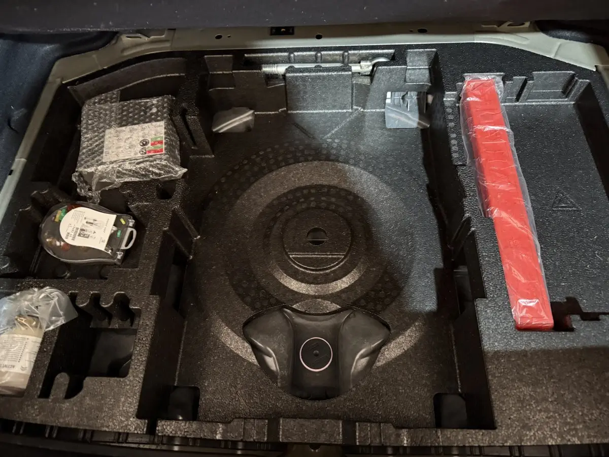 Vue rapprochée du compartiment de rangement sous le plancher de coffre de la Peugeot 308 noir, montrant les accessoires organisés.