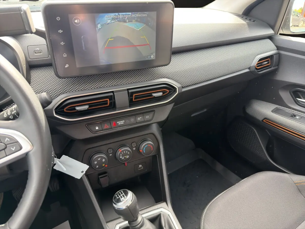 Vue intérieure côté passager de la planche de bord noire avec écran tactile et levier de vitesses manuel de la Dacia Sandero Stepway blanche.