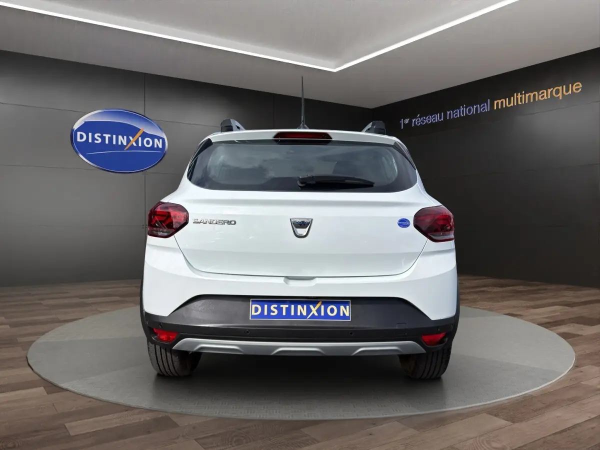 Vue arrière d'une Dacia Sandero Stepway blanche 2022 dans un showroom avec logo Distinxion en arrière-plan.