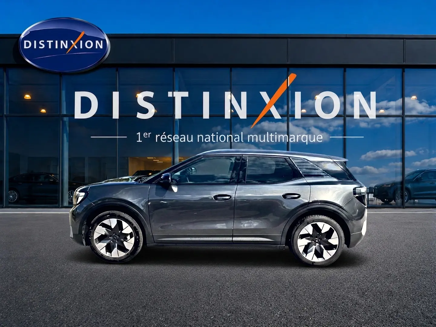 Vue latérale droite d'un Ford Explorer électrique gris métallisé 2025, avec jantes alu et vitres surteintées, devant une vitrine Distinxion.