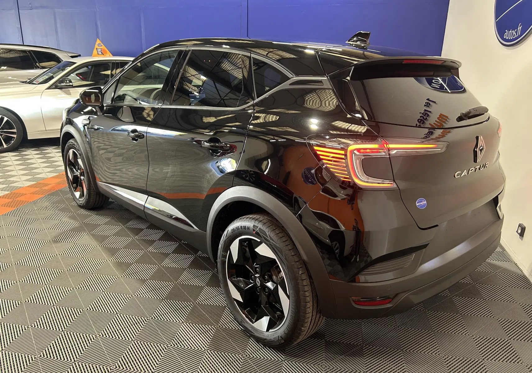 Renault Captur II Ph.2 TECHNO noir étoilé vu en 3/4 arrière droit, avec feux arrière allumés et jantes bicolores.