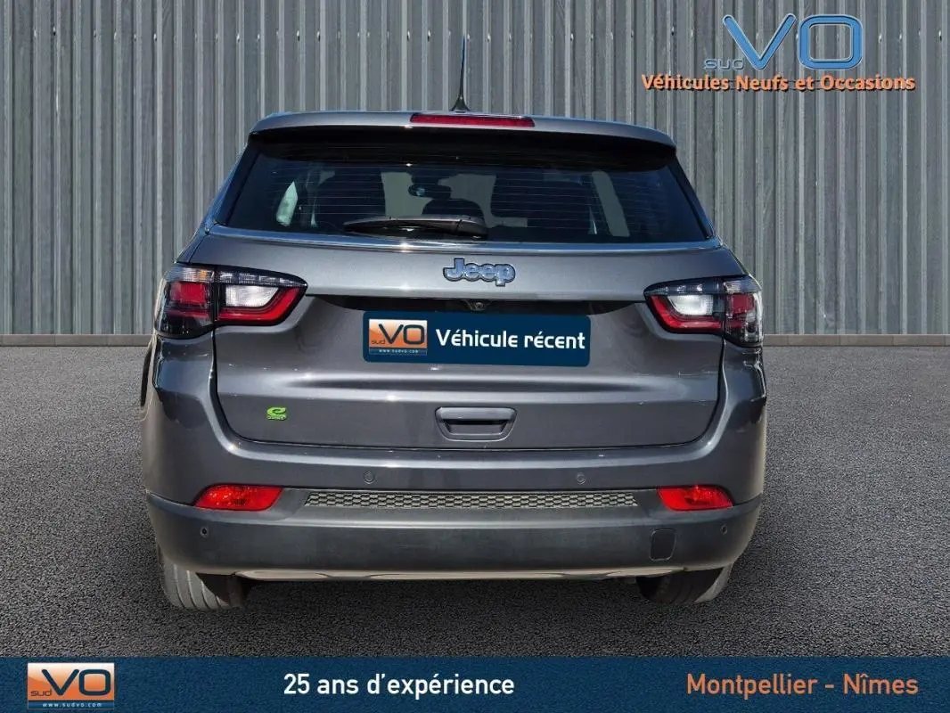 Vue arrière d'un Jeep Compass gris 2024 avec feux LED et logo e-Hybrid visible sur un parking.