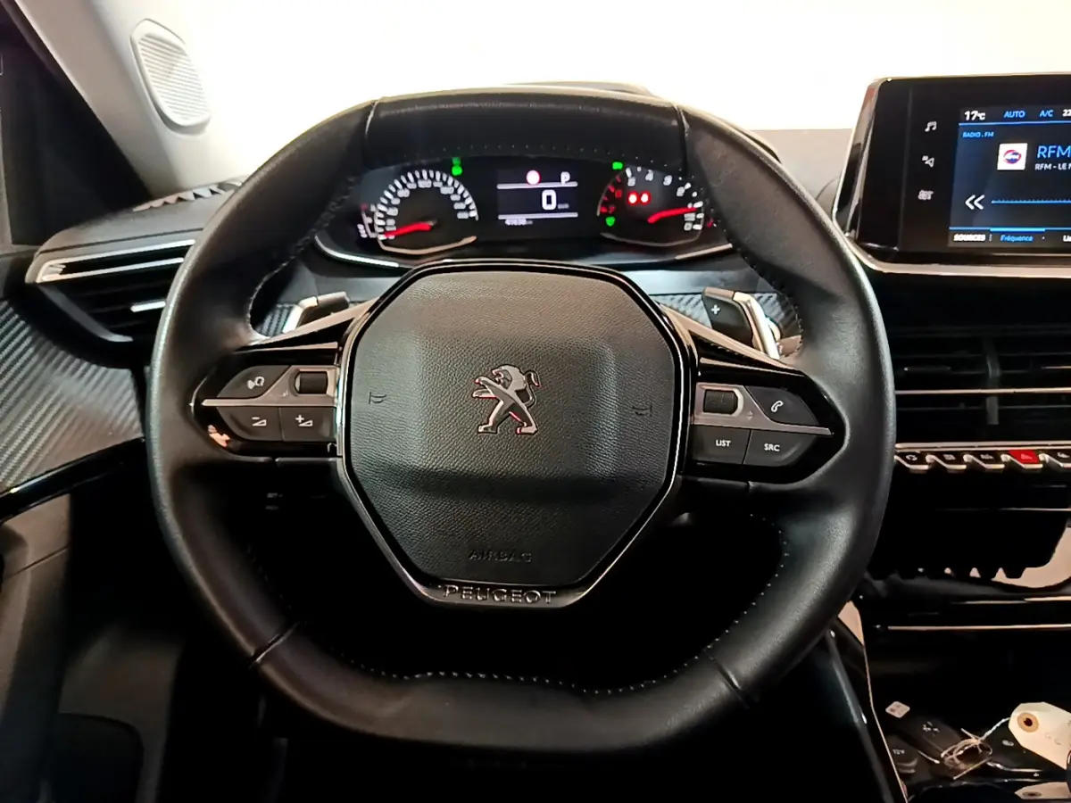 Vue rapprochée du volant cuir noir de la Peugeot 2008 2022 avec tableau de bord numérique et écran tactile central.