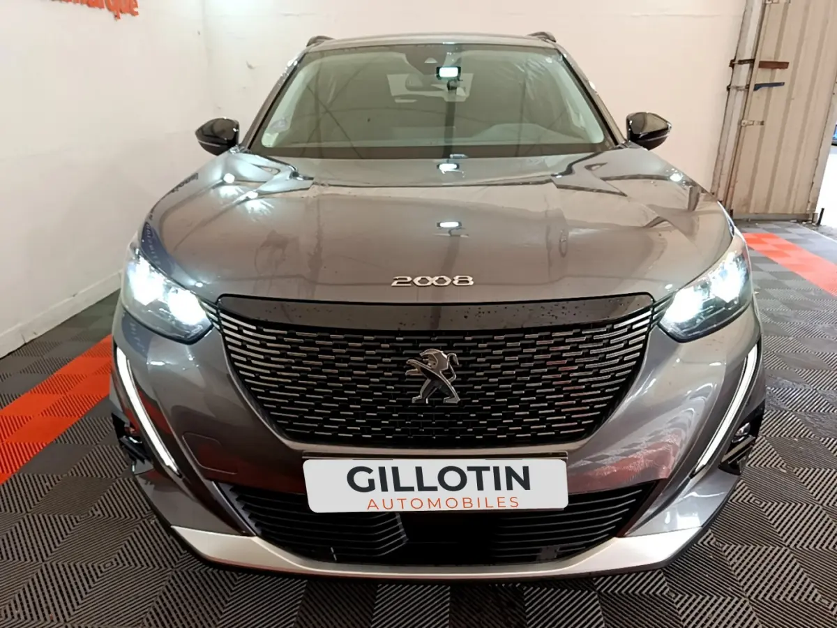 Vue avant d'un Peugeot 2008 gris foncé avec calandre noire et phares LED allumés en intérieur showroom.
