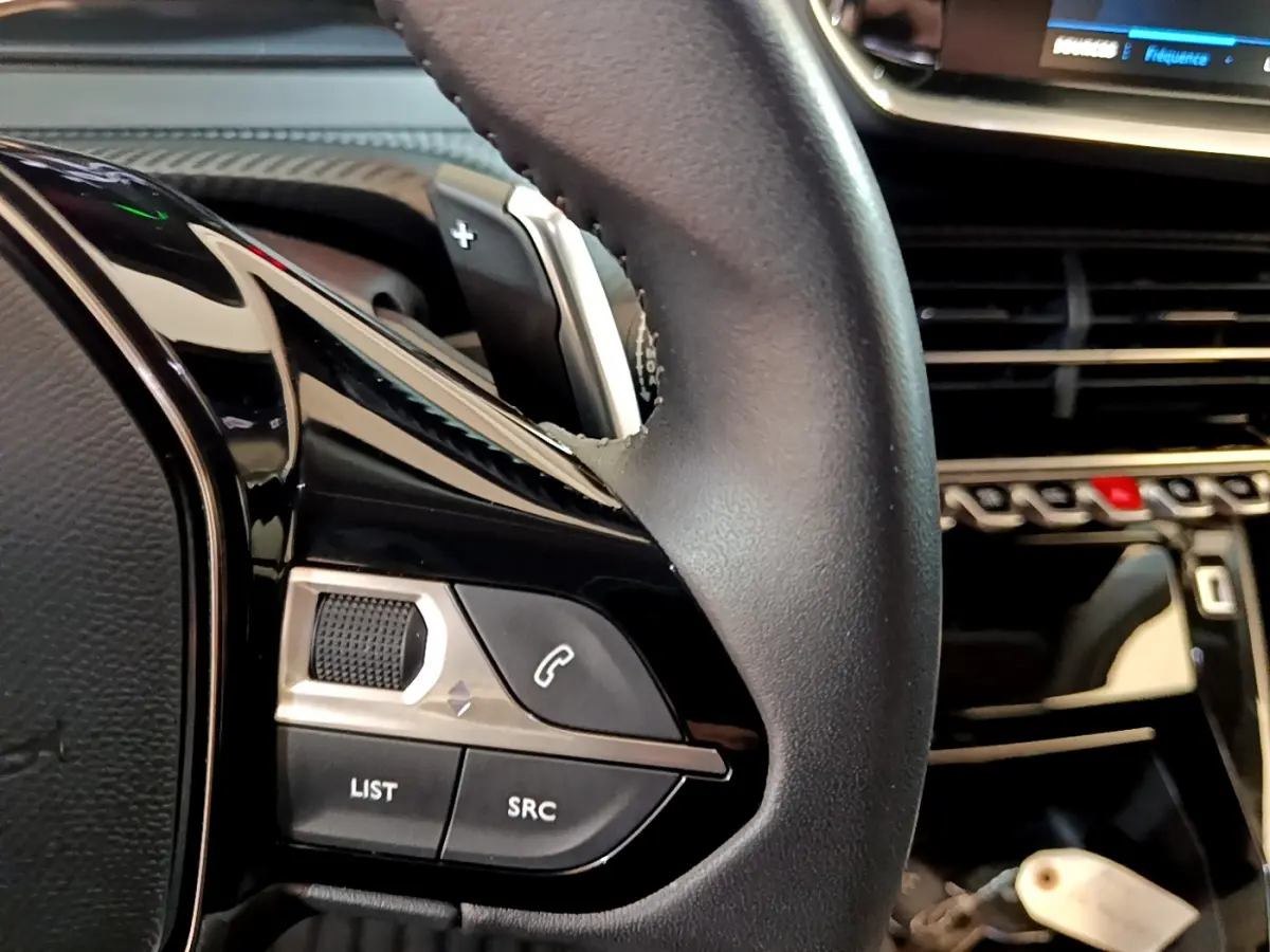 Gros plan sur le volant cuir noir du Peugeot 2008 2022, avec commandes audio et palettes au volant visibles.