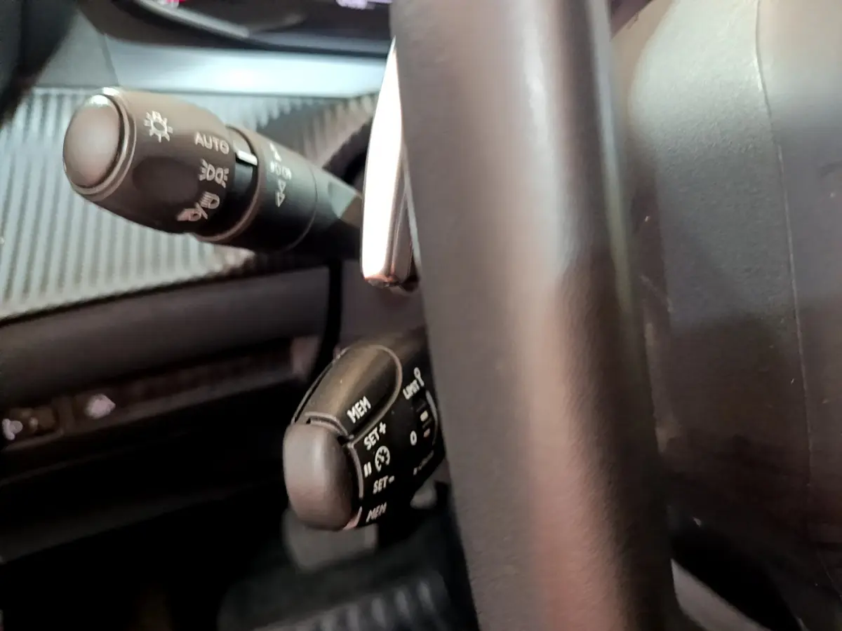 Gros plan sur les commandes au volant cuir noir du Peugeot 2008 2022, avec levier de clignotant et régulateur de vitesse.