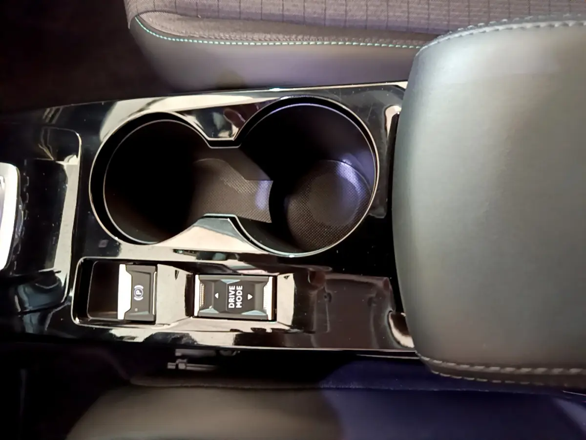 Gros plan sur la console centrale noire brillante du Peugeot 2008 gris foncé, avec porte-gobelets et boutons Drive Mode et frein électrique.