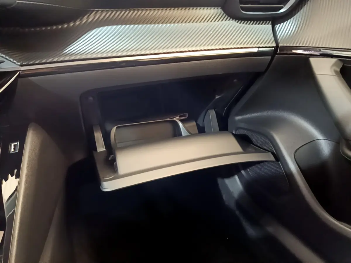 Gros plan sur la boîte à gants ouverte du Peugeot 2008 gris foncé, avec tableau de bord à finition carbone visible.