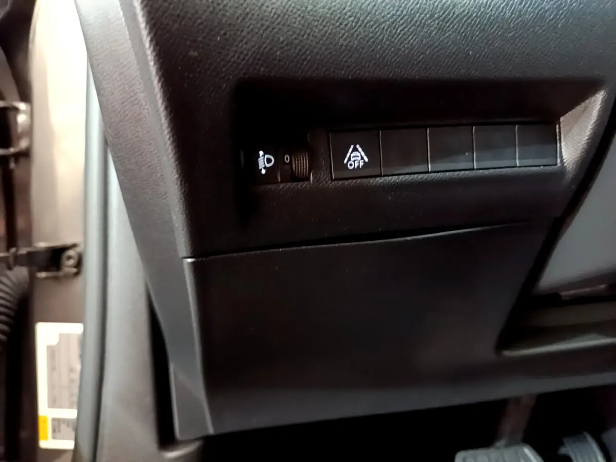 Gros plan sur les commandes de réglage des phares et d'alerte de franchissement de ligne à gauche du volant dans un Peugeot 2008 gris foncé 2022.