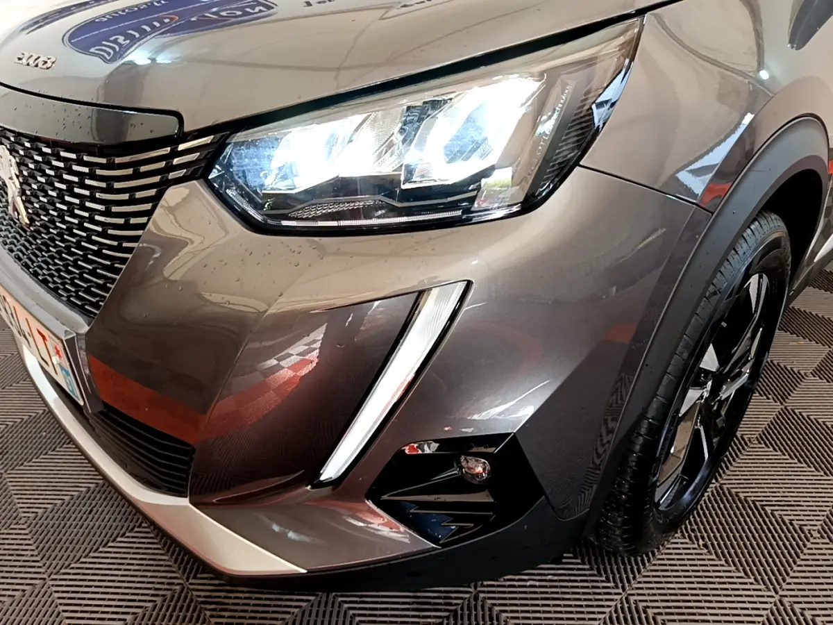 Gros plan sur l'avant droit d'un Peugeot 2008 gris foncé avec phares LED allumés et calandre distinctive.