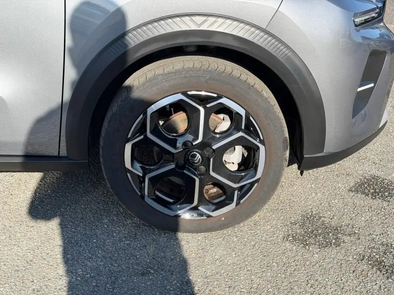 Gros plan sur la roue avant gauche d'une Citroën C3 2025 gris Mercury avec jante alu au design hexagonal noir et argent.
