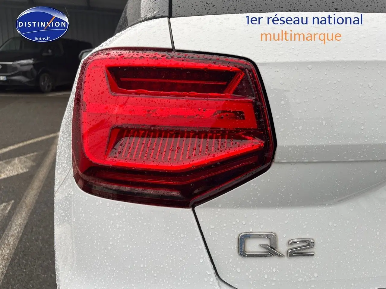 Gros plan sur le feu arrière gauche et le logo Q2 d’un Audi Q2 blanc Ibis sous la pluie.