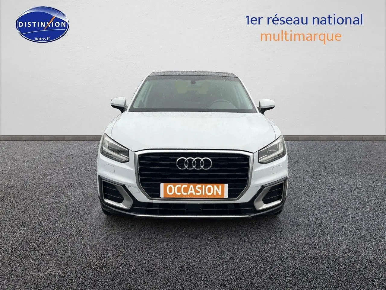 Vue frontale d'un Audi Q2 blanc Ibis avec calandre noire et plaque "OCCASION" orange visible.