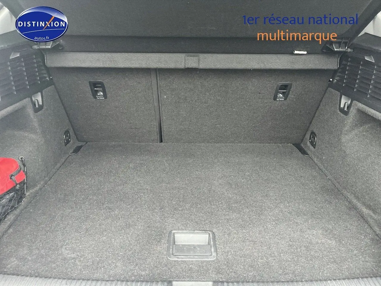 Coffre spacieux de l'Audi Q2 blanc Ibis, vue intérieure arrière avec tapis gris et filet de rangement rouge sur le côté.
