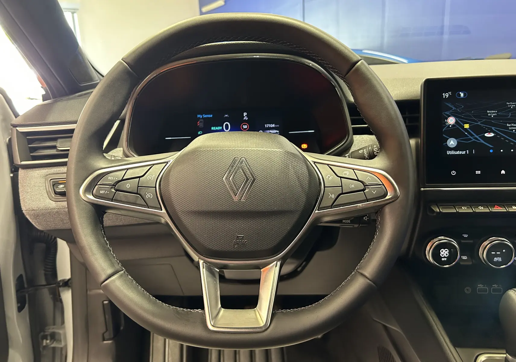 Vue rapprochée du volant en cuir noir avec logo Renault, tableau de bord digital et écran GPS à droite.