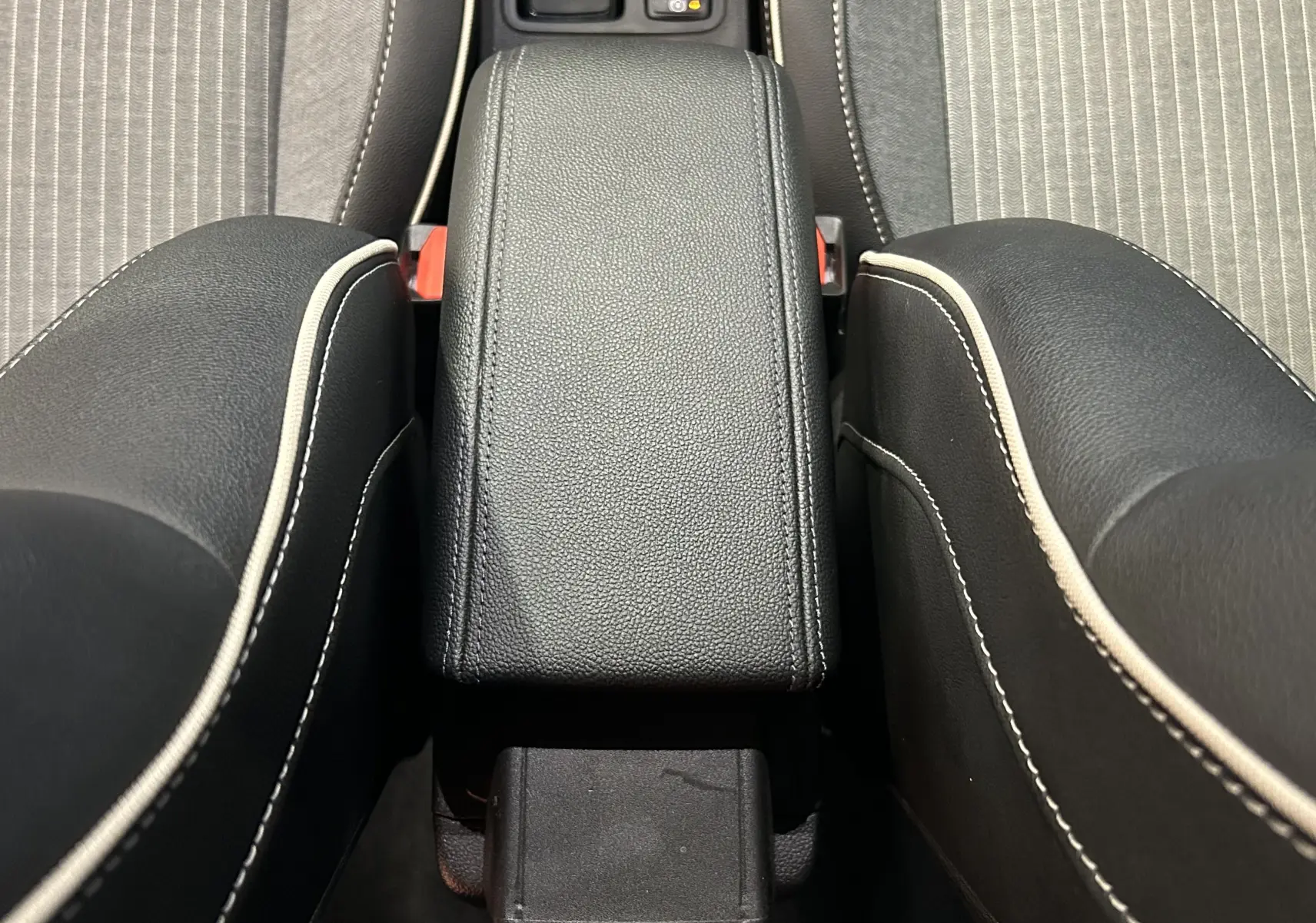 Vue rapprochée de l'accoudoir central en cuir noir avec surpiqûres blanches entre les sièges avant d'une Renault Clio V.