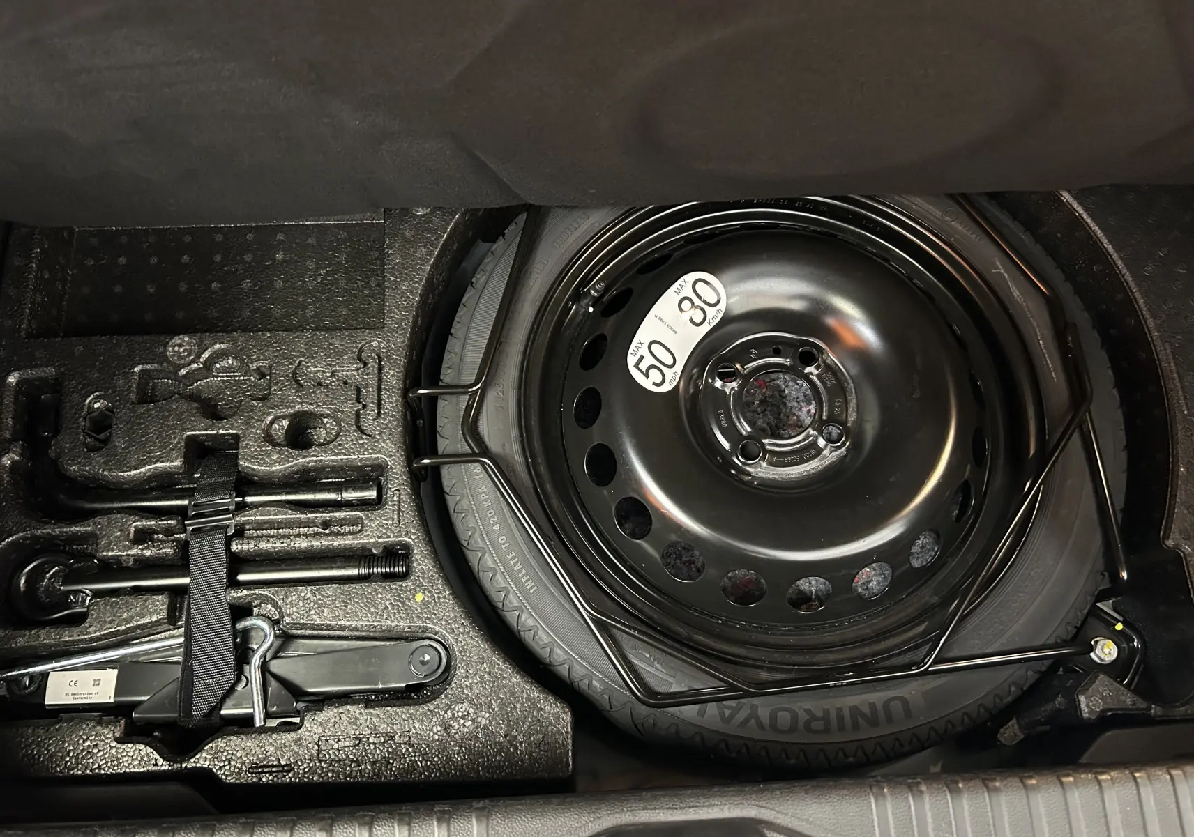 Vue rapprochée de la roue de secours noire et des outils de bord dans le coffre d'une Renault Clio V gris Rafale Métal.
