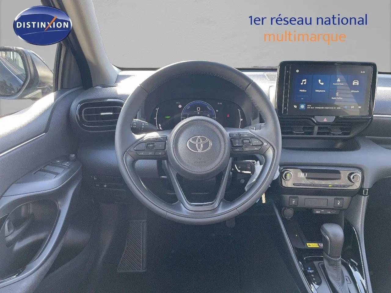 Vue intérieure avant centrée sur le volant et tableau de bord de la Toyota Yaris Hybrid 2025 en noir métal, avec écran tactile et commandes intégrées.