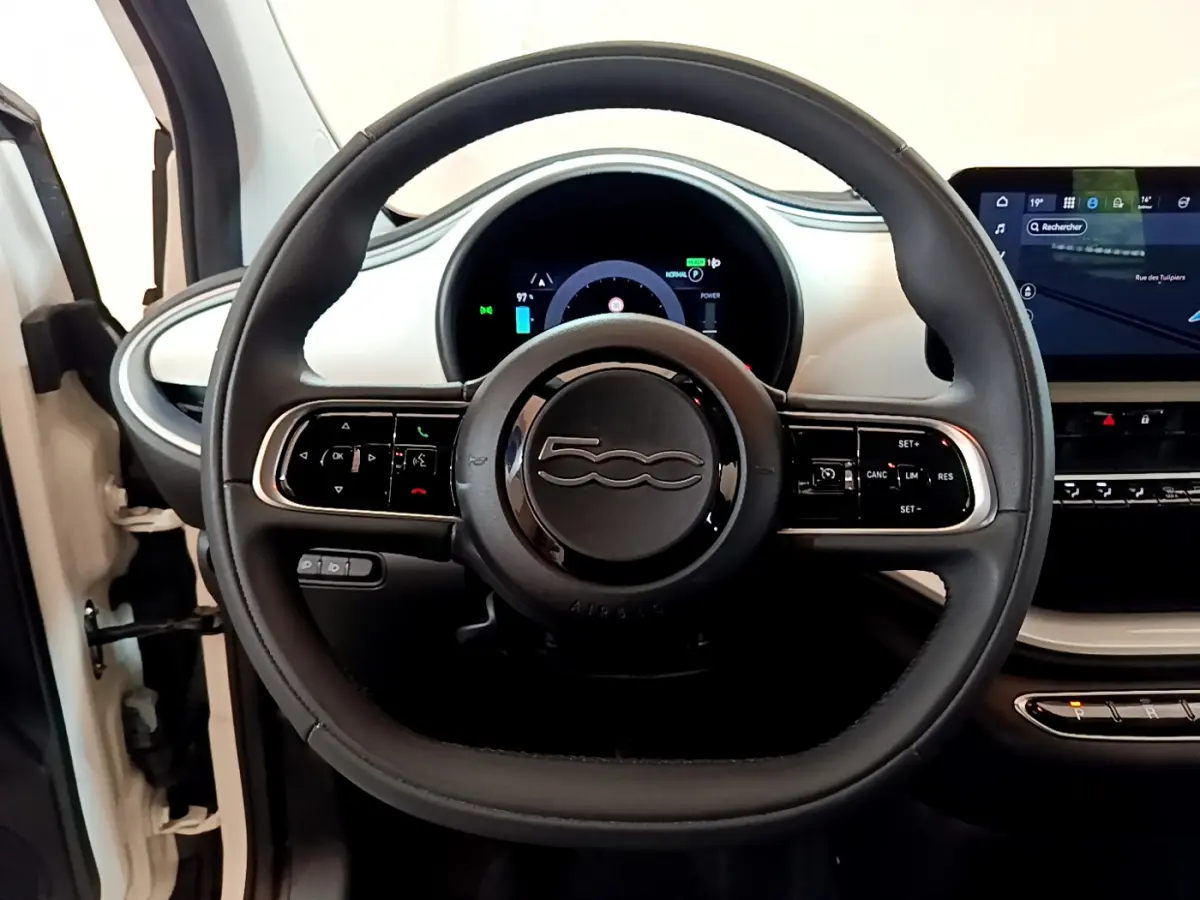 Vue rapprochée du volant noir de la Fiat 500 électrique blanche avec tableau de bord digital et écran tactile central.