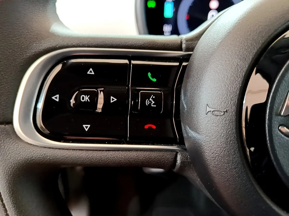 Gros plan sur les commandes gauche du volant cuir noir de la Fiat 500 électrique blanche 2022 Icône.