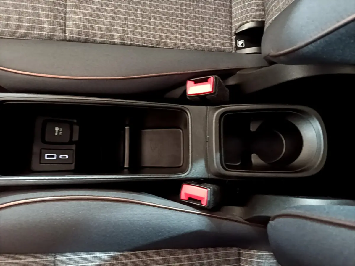 Gros plan sur la console centrale noire de la Fiat 500 électrique blanche, avec porte-gobelet et prises USB visibles entre les sièges.