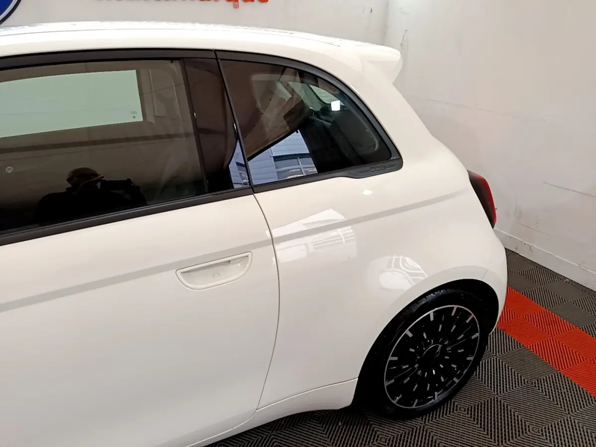 Vue latérale droite rapprochée d'une FIAT 500 électrique blanche avec jante noire et poignée de porte intégrée.