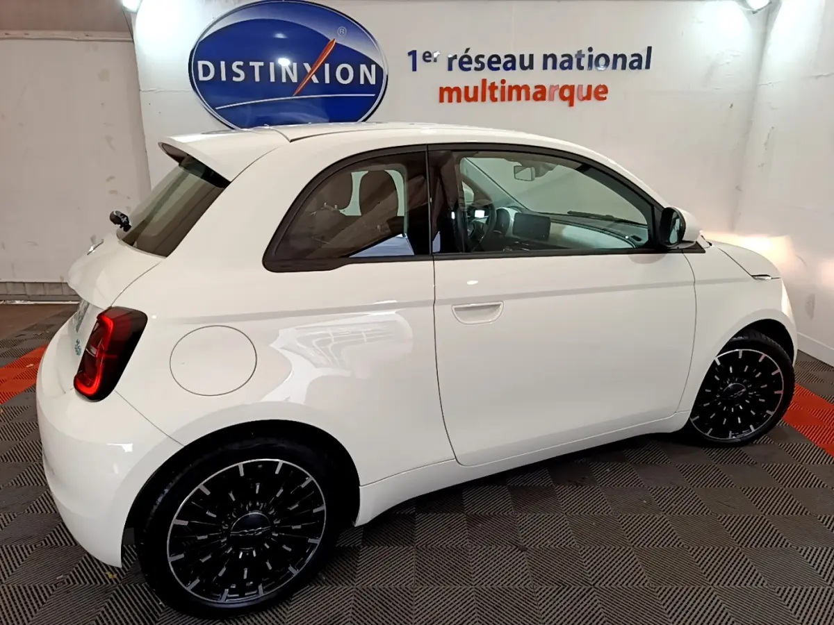Profil côté droit d'une FIAT 500 électrique blanche 42kWh Icône avec jantes noires et vitres teintées en intérieur showroom