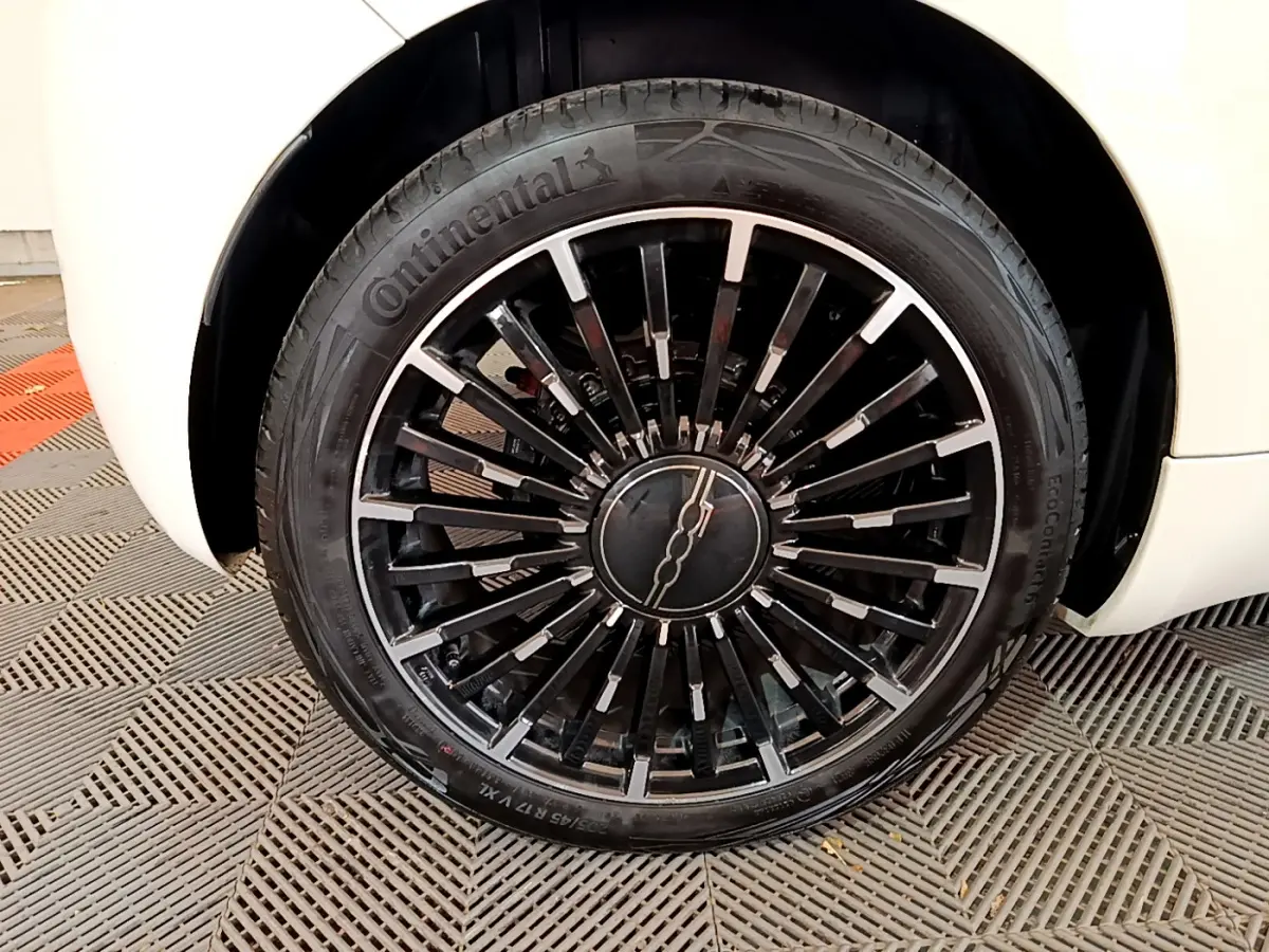 Gros plan sur la roue avant droite noire et argentée d'une FIAT 500 blanche 42kWh Icône électrique 2022.