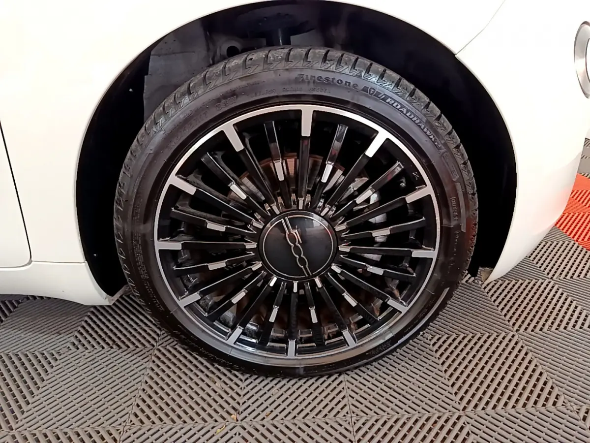 Gros plan sur la roue avant droite noire à jante stylisée du Fiat 500 blanc électrique 42kWh Icône 2022.