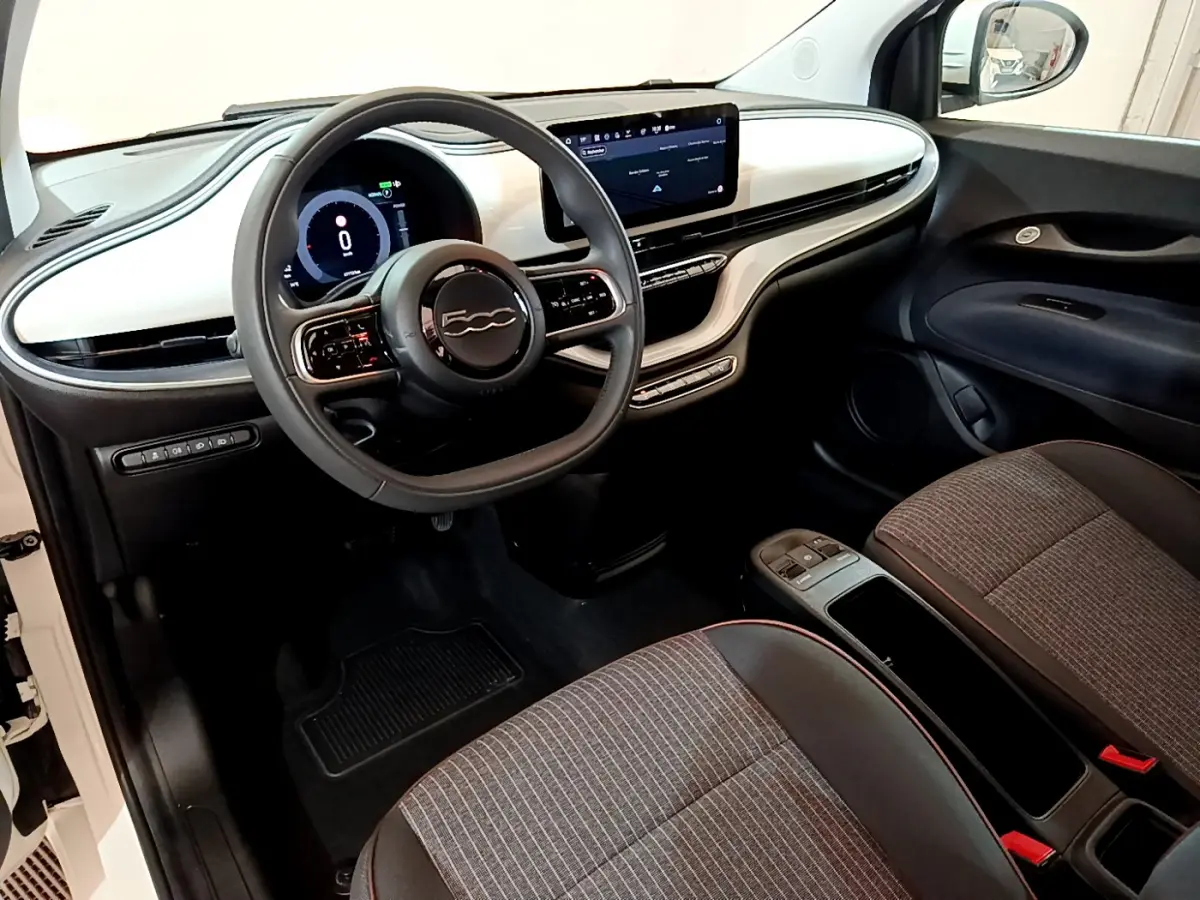 Intérieur avant de la Fiat 500 électrique blanche, vue côté conducteur, tableau de bord moderne avec écran tactile central.