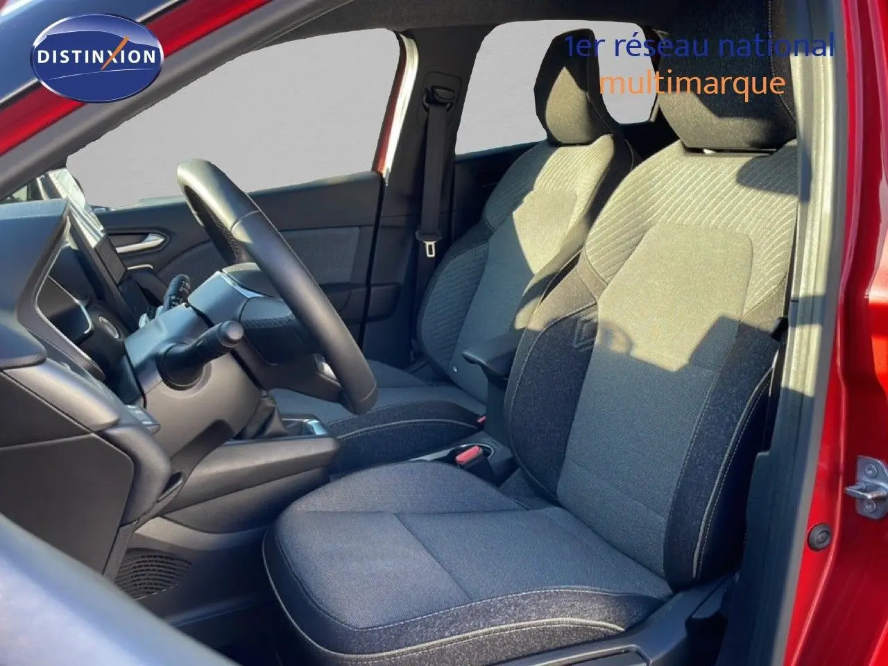 Vue intérieure côté conducteur du Renault Captur rouge désir métal, montrant les sièges en tissu gris et le volant.