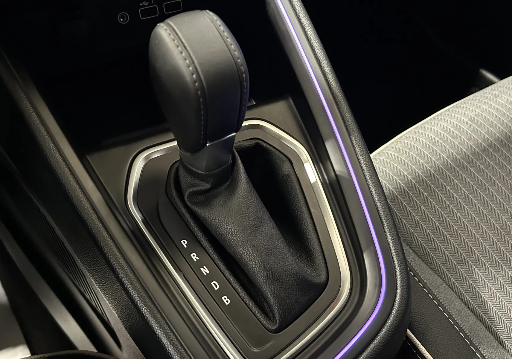 Gros plan sur la commande de boîte automatique noire avec surpiqûres, entourée d’un éclairage d’ambiance violet dans une Renault Clio V.