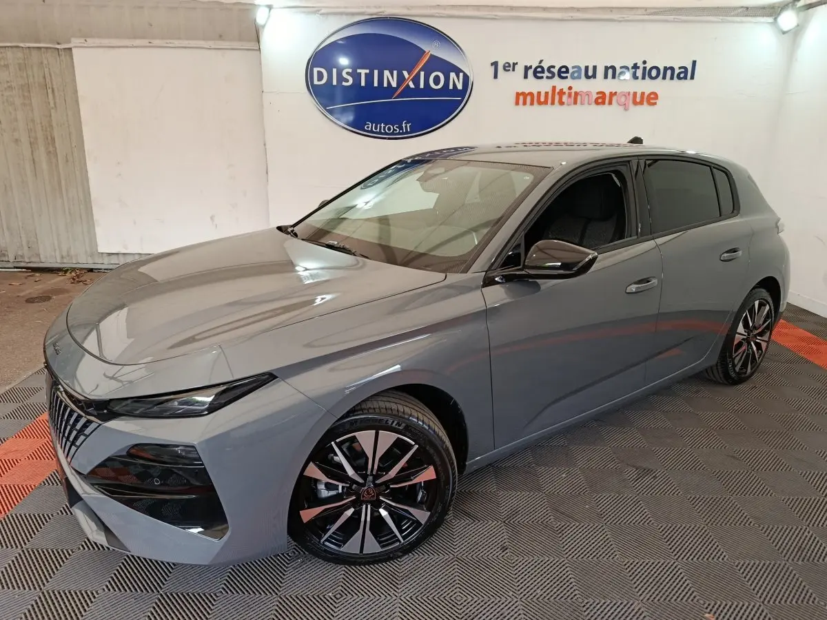 Peugeot 308 gris foncé vue 3/4 avant droit, avec jantes alliage noires et calandre distinctive en intérieur showroom.