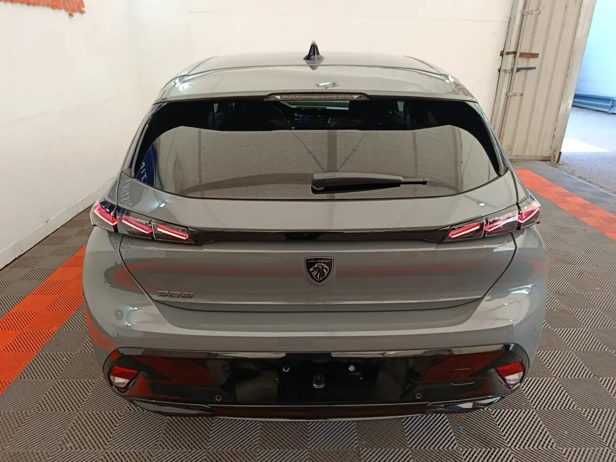Vue arrière d'une Peugeot 308 gris foncé 2026 avec feux LED et lunette arrière teintée dans un garage.