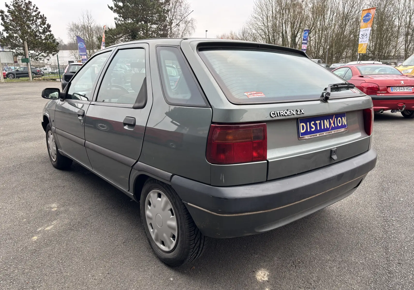 Vue 3/4 arrière droite d'une Citroën ZX gris 1992 avec plaques Distinxion et feux arrière rouges.