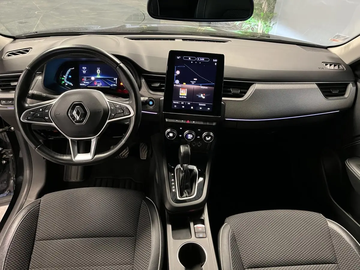 Vue intérieure avant du Renault Arkana 1.6 E-Tech Hybride 2021, tableau de bord noir avec écran tactile vertical et volant cuir.