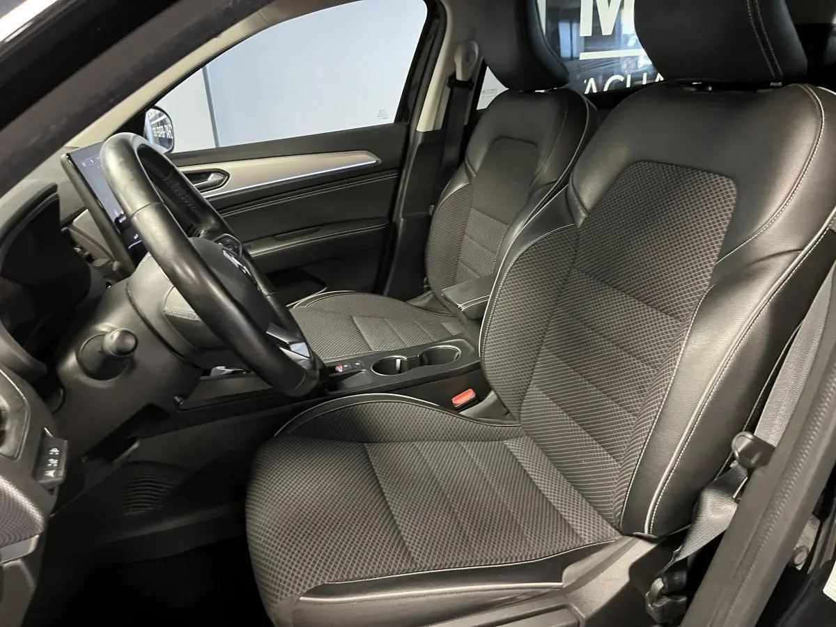 Intérieur avant droit du Renault Arkana noir, sièges tissu/similicuir noirs avec volant cuir et console centrale visible.