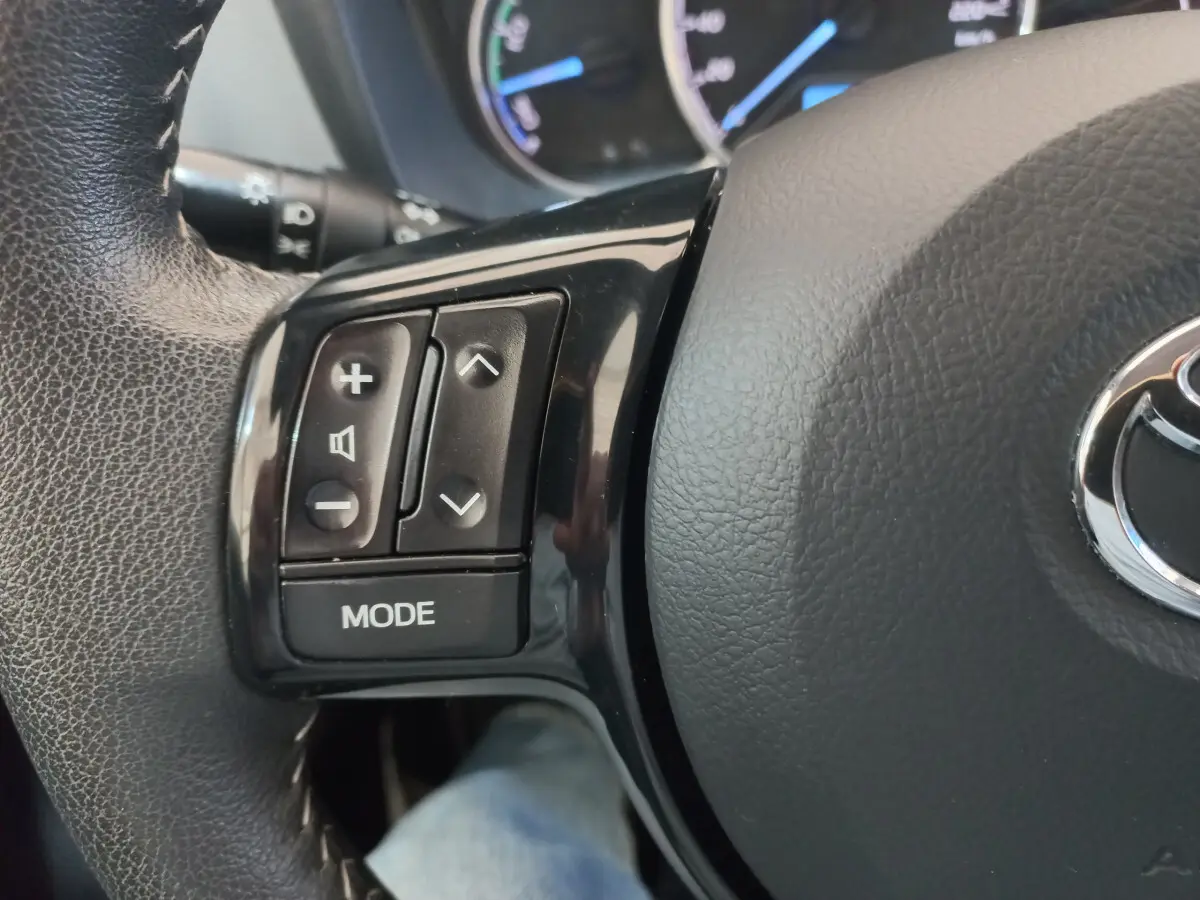 Gros plan sur les commandes gauche du volant cuir noir de la Toyota Yaris hybride blanche de 2019.