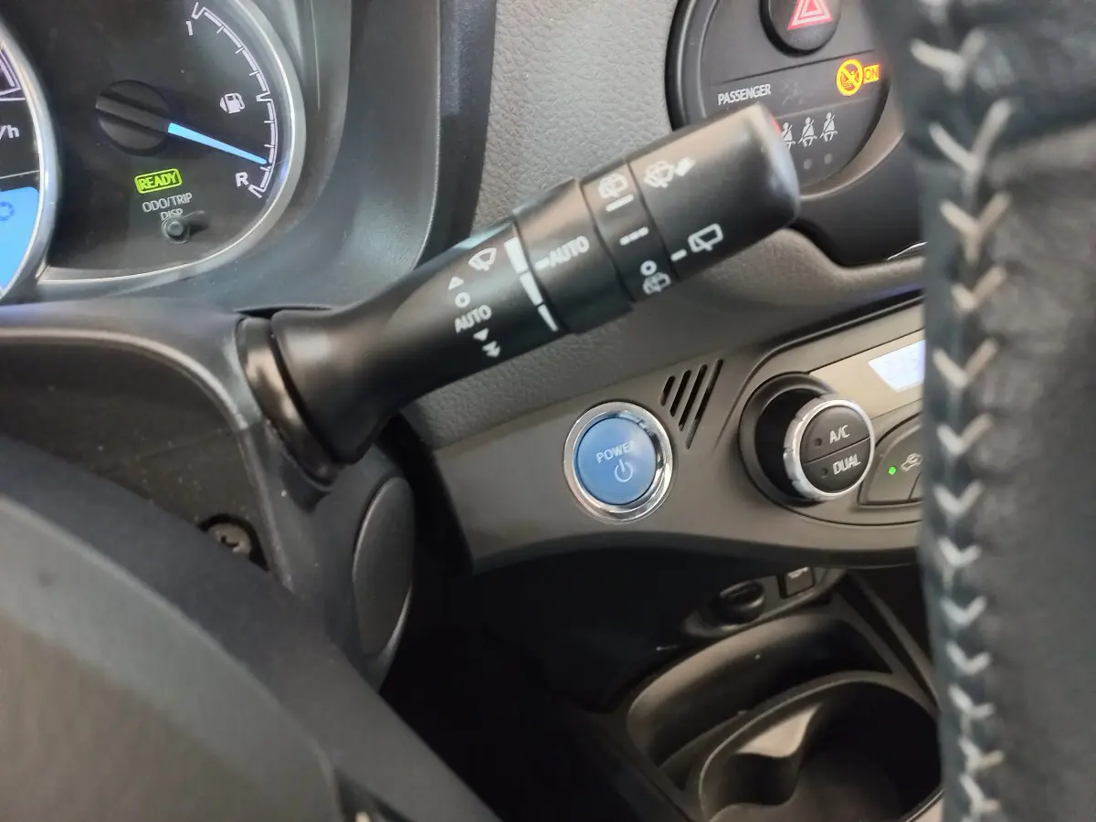 Détail intérieur montrant le bouton Power bleu, commandes climatisation et partie du volant cuir de la Toyota Yaris hybride blanche.