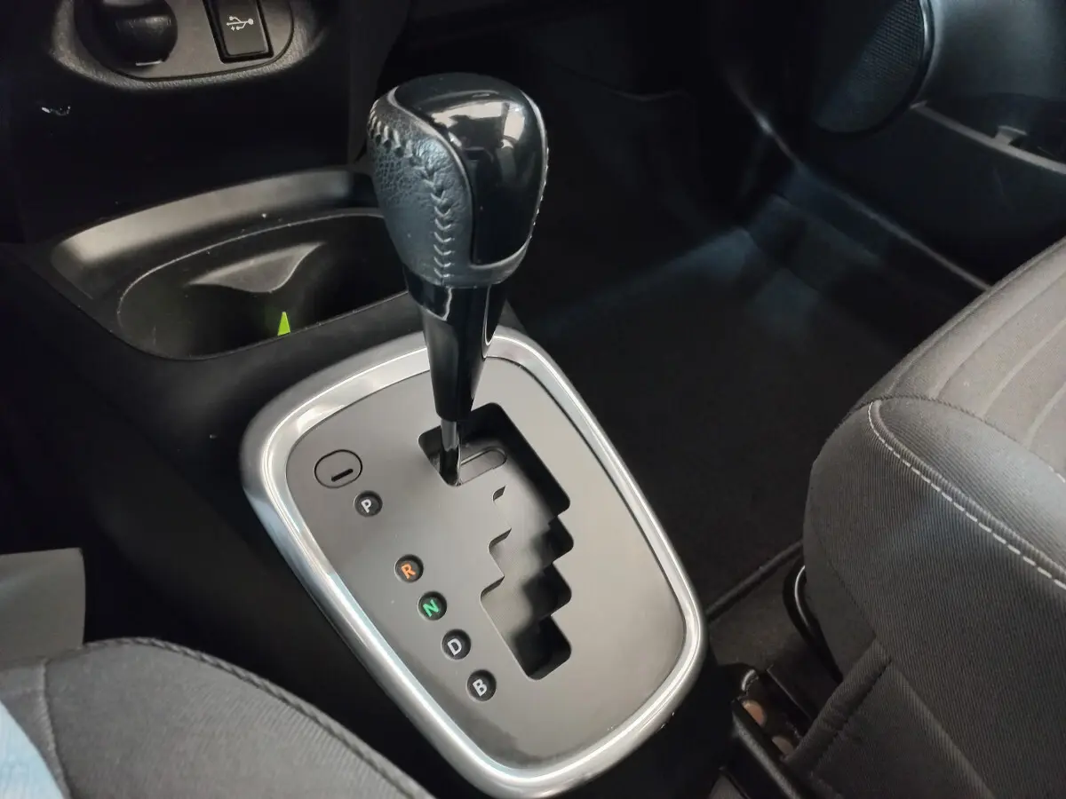 Le levier de boîte automatique noir vu de dessus dans l'habitacle sombre de la Toyota Yaris hybride blanche.