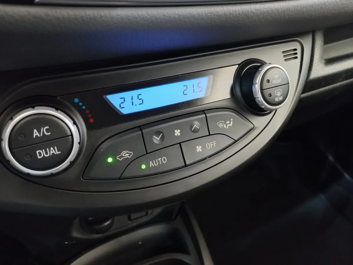 Gros plan sur la commande de climatisation bi-zone digitale de la Toyota Yaris hybride blanche, affichant 21,5°C.